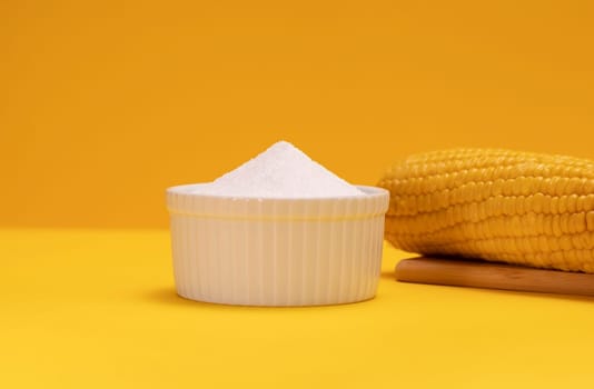 Erythritol, organic sweetener produced by fermentation from corn, called dextrose in ceramic bowl on yellow orange background, bunch of corn. Sugar substitute. Horizontal plane, copy space for text.