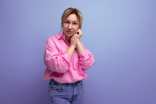 well-groomed young blond caucasian woman model with a ponytail hairstyle put on a pink shirt and jeans and poses against the background with copy space.