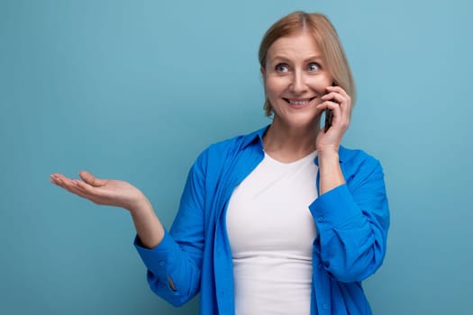 middle aged woman chatting using smartphone on blue background copy space.