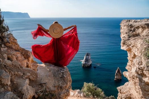 A woman in a flying red dress fluttering in the wind and a straw hat against the backdrop of the sea