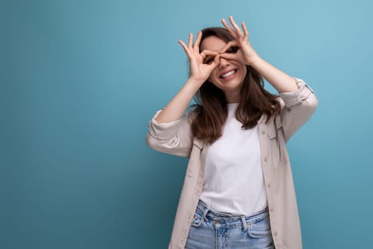 cheerful cute 30s dark haired woman in shirt and jeans with grimace on blue background.