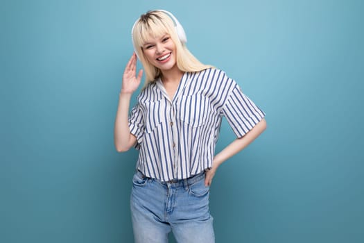 energetic blonde young female adult in blouse with headphones isolated background.