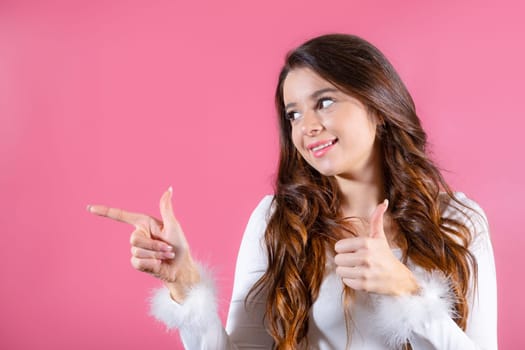 A youthful woman beaming with happiness looks to the right and shows on copy space on a vivid pink background. Emotional advertisement concept