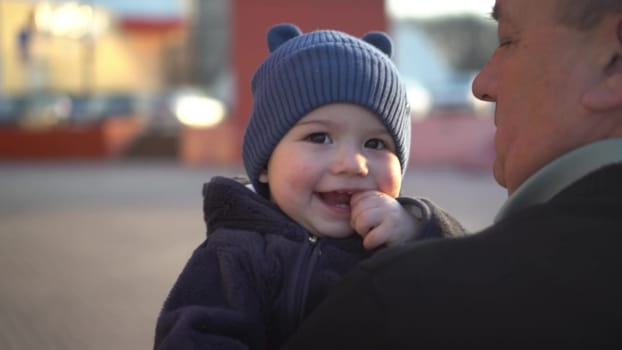 A small child in the arms of a grandfather. A boy in the arms of a man walks down the street. 4k