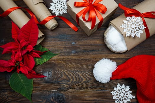 The concept of preparing for the Christmas holiday. Flatley. View from above. On a wooden table there are items for preparing for Christmas - a stollen, wrapping paper for gifts, a gift, a Santa hat, pointessia