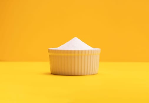 Natural organic sweetener Erythritol, produced by fermentation from corn, called dextrose in ceramic bowl on yellow orange background. Sugar substitute. Horizontal plane, copy space for text.