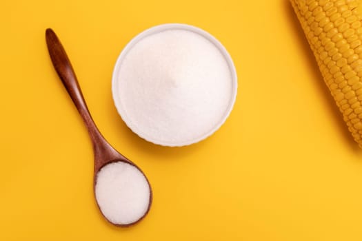 Organic sweetener Erythritol, produced by fermentation from corn, called dextrose in ceramic bowl, wooden spoon, corncob on yellow orange background. Sugar substitute. Horizontal plane, top view.