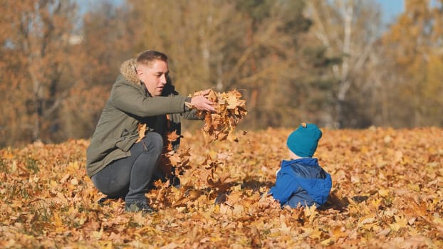 A happy father sprinkles leaves on his son