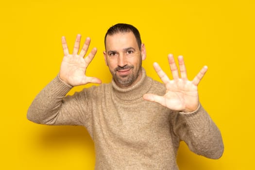 Front view of a Hispanic man with short hair wearing a beige turtleneck with his palms in front of him, camera facing palm, touching an interactive virtual screen