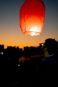 silhouette of man pushing up paper sky lantern with flame at bottom at sunset on sankranti uttarayan, independence day India