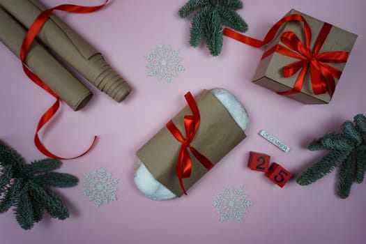 The stollen wrapped in craft paper lies on a pink background, there is paper around for wrapping gifts, a gift and branches of nobiles