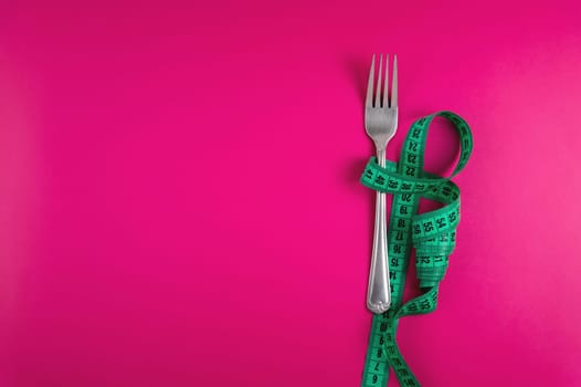 Fork wrapped with a measuring tape on a colored background. Bright background for advertising. Weight control, slimming and health concept.