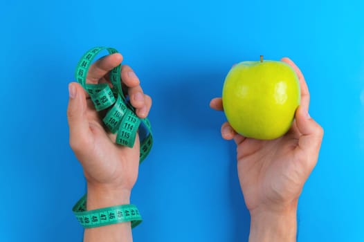 Diet concept. Male hands hold a green apple against the background of a measuring tape, a choice in favor of a healthy diet. View from above.