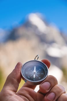 A man holds a compass in his hand against the backdrop of mountains, blurred background, close-up. concept of travel and navigator on vacation.