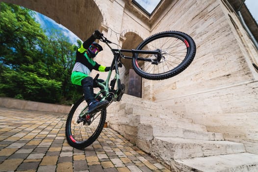 Active young biker jumping on the rear wheel of a mountain bike. Extreme sport. Wide angle front view of a cyclist. Focused sportsman is preparing for a stunt in the city. The athlete holds a mountain bike and stands on one wheel. The concept of maintaining balance.
