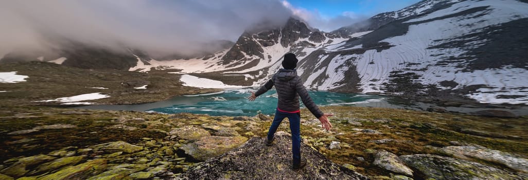 Beautiful mountain landscape with a lake and an emotional man. Sports extreme. The traveler man spread his arms, standing alone on the stone. emotional adventure concept, outdoor activity wild scandinavian nature.