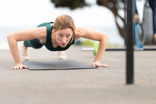 Adult sportive woman with no make up doing push ups outdoors. Mid shot