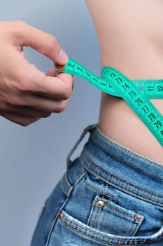 Waist of a slim woman in jeans. Close-up of a slim woman measuring the size of her waist with a tape measure.