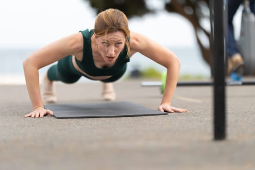 Adult athletic woman with no make up doing push ups outdoors. Mid shot