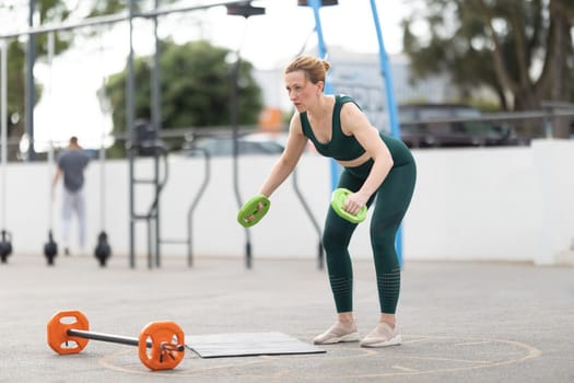 Adult athletic woman with exercising outdoors - training her arms lifting weights. Mid shot