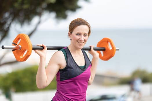 Adult athletic smiling woman with no make up with a dumbbell on her shoulders. Portrait
