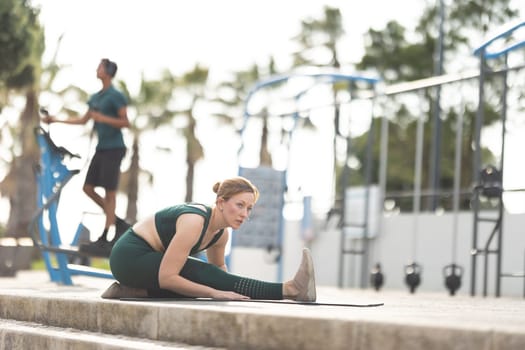 Adult woman doing stretching exercises outdoors on yoga mat. Mid shot