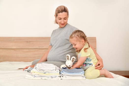 Mother and daughter together prepare clothes for a newborn boy