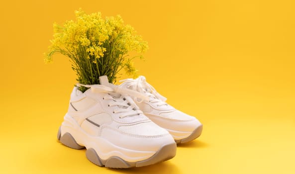 White Sneakers, Streetwear With Yellow Flowers On Yellow Background. Monochrome Minimalism. Copy Space For Text. Creative Fitness. Eco Leather Shoes. Deodorant For Shoes Concept. Horizontal Plane.
