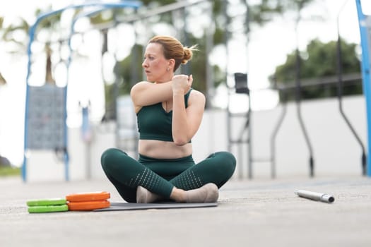 Adult athletic woman exercising outdoors - sitting in lotus position and warming up. Mid shot