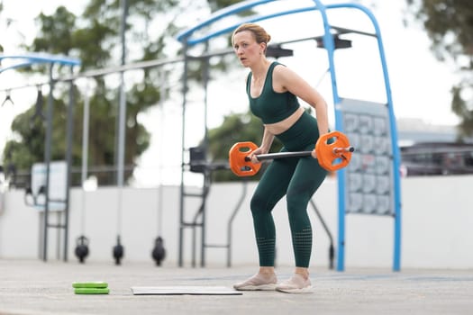 Adult athletic woman exercising outdoors - lifting a dumbbell. Mid shot