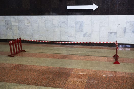 Photo of arrow to right against background of marble wall in subway. Wooden fences. Prohibition of passage. Damaged floor covering.