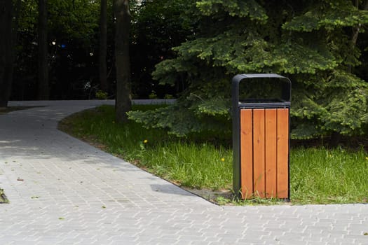 Photo of wooden trash can next to path in park. Garbage collection. Environment protection. Politeness.