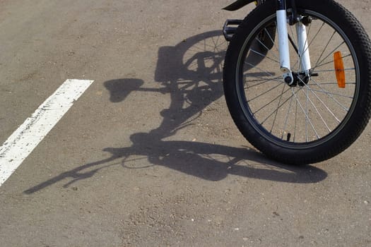 Photo of bicycle shadow on gray asphalt. Sunny day. Front wheel with spokes.