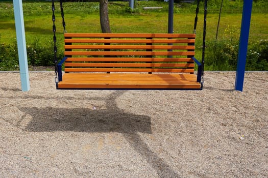 Photo wooden bench swing suspended. Place for rest. Park, square. Walk with children.