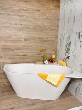 Modern ceramic bathtub with yellow towel in room. White tub in minimalistic bathroom interior. Porcelain bathtub with classic design in comfortable apartment or hotel room. home decor in spa center