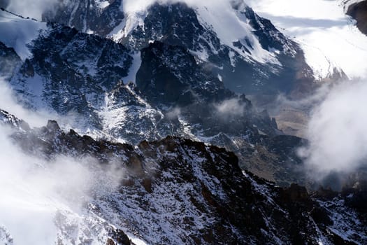 Highlands cliffs, snow-capped peaks of mighty mountains in the clouds, a stunning view from above