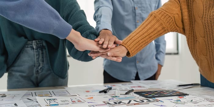 A close-up image of a team of developers or graphic designers putting their hands together at working table in office.
