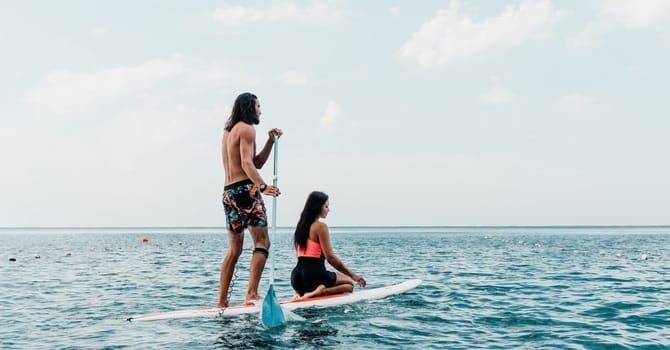 Sea woman and man on sup. Silhouette of happy young woman and man, surfing on SUP board, confident paddling through water surface. Idyllic sunset. Active lifestyle at sea or river