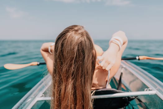 Woman in kayak back view. Happy young woman with long hair floating in transparent kayak on the crystal clear sea. Summer holiday vacation and cheerful female people having fun on the boat.