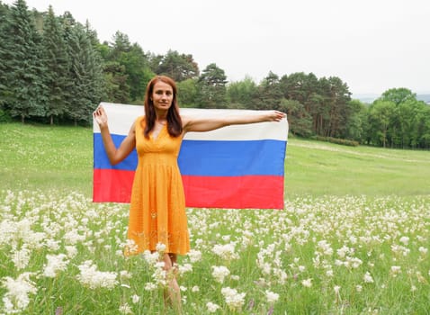 Young woman in a yellow dress with the national flag of Russia outdoors in a flowering field