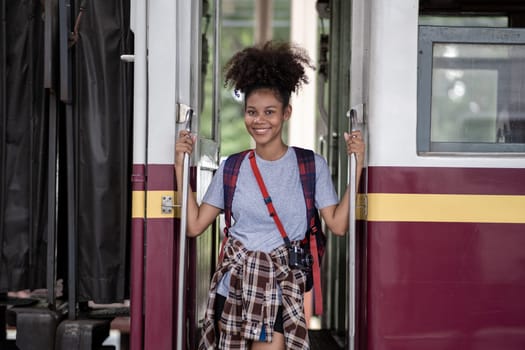 Traveler African Asian American woman getting in a train to hop on train, Young woman female standing on train door peeking out looking from door, tourist on a train station. High quality photo