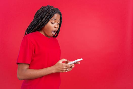 Surprised african woman looking the screen of a mobile in studio with red background