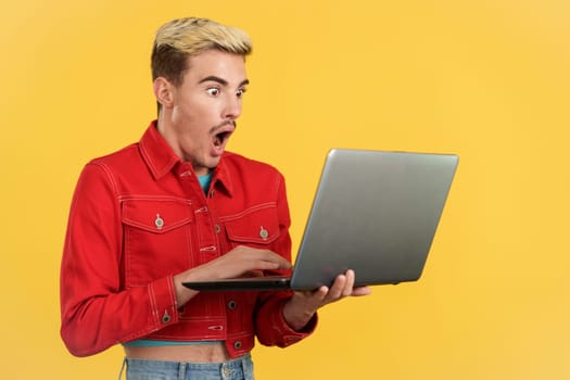 Stylish surprised gay man using a laptop in studio with yellow background