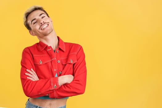 Cheerful gay man posing with arms crossed in studio with yellow background