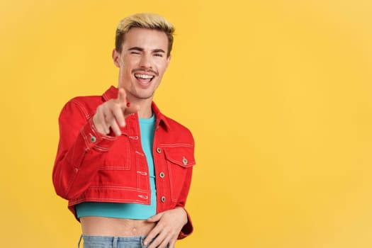 Stylish gay man laughing while pointing ahead in studio with yellow background