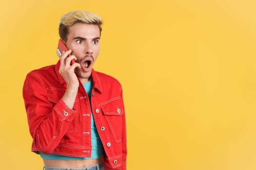 Surprised gay man talking to the mobile phone in studio with yellow background