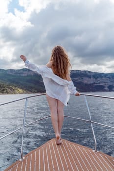 Woman on a yacht. Happy model in a swimsuit posing on a yacht against a blue sky with clouds and mountains.