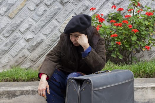 unhappy retired woman with suffering, emotional stress and depression sitting on the street next to an old gray suitcase. High quality photo