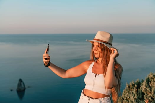 Selfie woman in hat, white tank top and shorts makes selfie shot mobile phone post photo social network outdoors on sea background beach people vacation lifestyle travel concept