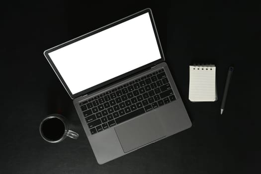 Above view of laptop with empty display, notepad and coffee cup on black background.